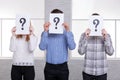 Two guys and a girl stand side by side close their faces with sheets with question marks close-up