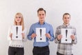 Two guys and a girl with light smiles are standing next to keep the sheets with exclamation marks on a gray background Royalty Free Stock Photo