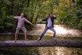 Two guys play funnily fighting in martial arts style on a log bridge