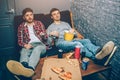 Two guys sitting on the couch and holding some food and drinks in their hands. They feel relaxed and tired after a long Royalty Free Stock Photo