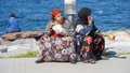 Two Gypsy women sit on the pavement of seaside