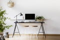 Two hairpin stools placed by black desk with metal lamp, fresh plant and mockup monitor in real photo of white living room interio Royalty Free Stock Photo