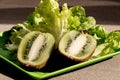 Two half juicy ripe kiwi fruit, fresh lettuce on plastic plate. Green background. Salad leaves. Organic healthy food. Detox diet Royalty Free Stock Photo