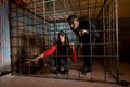 Two Halloween victims imprisoned in a metal cage, girl pulling h