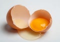 Two halves of a broken brown eggshell on a white surface with a bright yellow yolk contained in one Royalty Free Stock Photo
