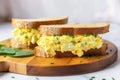 two halves of egg salad sandwich on a walnut board