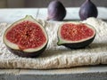 Two halves of figs cut in half lie on a wooden table on a linen napkin. In the background are two more fig berries. Front view.