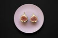 Two halves of fresh fig on pink plate over black surface, top view. Flat lay, overhead, from above