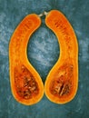Two halves of a pear-shaped pumpkin of orange color, are located on a background of turquoise color vertically