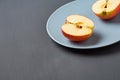 Two halves of red fresh ripe apples full of vitamins lies on circle ceramic plate and old dark scratched concrete table on kitchen