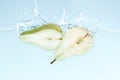 Two halves of yummy green pear flying into water with splash on blue background Royalty Free Stock Photo