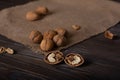 Two halves of a walnut lie on a wooden table in the foreground. Whole walnuts lie on linen cloth.