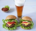 Two hamburger with beef patty, with cheese, pickles, tomatoes, onions, lettuce and tomato sauce in a saucer with a glass of beer Royalty Free Stock Photo