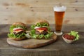 Two hamburger with beef patty, with cheese, pickles, tomatoes, onions, lettuce and tomato sauce in a saucer with a glass of beer o Royalty Free Stock Photo