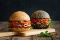 Two hamburgers with sesame seeds with fresh vegetables tomato, bell pepper, spicy carrots, parsley and ham, light and dark, on a