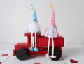 Two hand-made gnomes in love are sitting on a wooden red car on a light background