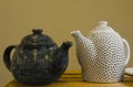 Two handmade teapots on a wooden shelf in the market. White ceramic teapot in the black dot. Dark teapot. Royalty Free Stock Photo