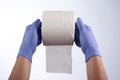 Two hands in blue gloves holding with index fingers a roll of toilet paper Royalty Free Stock Photo