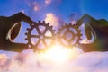 Two hands connect the gears, the details of the puzzle. against the sky with sunset. Royalty Free Stock Photo