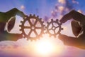 Two hands connect the gears, the details of the puzzle. against the sky with sunset. Royalty Free Stock Photo