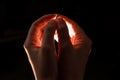 Two hands folded squeeze the light inside, reddish light inside the hands, black background. Royalty Free Stock Photo