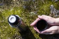 Two hands hold cup of hot tea or coffee on mossy rock