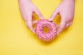 Two hands hold a pink donut. Yellow background