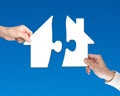 Two hands holding jigsaw pieces to finish house shape puzzle