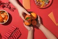 Two hands are holding a plate of tangerines, a string of red firecrackers, a branch of peach blossoms, lucky money envelopes and a Royalty Free Stock Photo