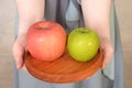 Two hands holding a wooden plate containing red apple and green apple