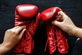 two hands lacing up red boxing gloves