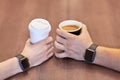 Two hands, male and female, both with equal electronic wrist watches, holding cups of coffee, white and black, on the wooden table Royalty Free Stock Photo