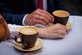 Two hands, male and female, with the wedding rings touch of brown coffee cup Royalty Free Stock Photo