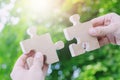 Two hands person trying to connect couple Jigsaw wooden puzzle piece with tree fresh background. one part of whole. Royalty Free Stock Photo