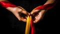 Two hands pulling red and yellow satin ribbons on black background. World Hepatitis Day.