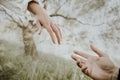 Two hands reach helping each other Against the background of a tree and grass