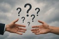 Two hands reaching with floating question marks against cloudy sky symbolizing confusion and inquiry Royalty Free Stock Photo