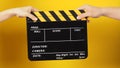 Two hands send and hold a Black clapper board or movie slate on yellow background