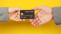 Two hands send and hold a Black credit card on yellow background. Arms wear a grey suit