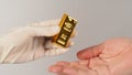 Two hands send and recive gold bar on white background. One Hand wear latex glove