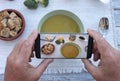 Two hands take a mobile photo of a creamy homemade vegetable soup fresh and ready to eat. Made with cauliflower potatoes, peas, Royalty Free Stock Photo