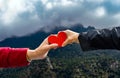 Two hands touching each other making a heart shape and holding a figure of a red heart with a mountainous and cloudy background of Royalty Free Stock Photo