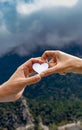 Two hands touching each other making the shape of the heart and holding a figure of a white mockup heart with a mountainous and Royalty Free Stock Photo