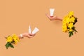 Two hands with yellow chrysanthemums holding white tubes of cream or gel and small pump bottle without logo. Blank