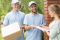 Handsome couriers in blue uniforms delivering a parcel to a young pretty woman