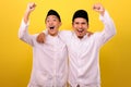 Two handsome happy Asian Muslim men hugging and looking at camera with satisfied amazed face while showing winning gesture Royalty Free Stock Photo