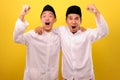 Two handsome happy Asian Muslim men hugging and looking at camera with satisfied amazed face while showing winning gesture Royalty Free Stock Photo