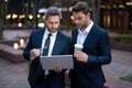 Two handsome young businessmen in classic suits using laptop. Business men team using laptop outdoor. Businessmen Royalty Free Stock Photo