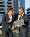 Two handsome young businessmen in classic suits using laptop. Businessmen outdoors near city cityscape using laptop Royalty Free Stock Photo