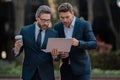 Two handsome young businessmen in classic suits using laptop. Freelance concept. Business men team using laptop outdoor Royalty Free Stock Photo